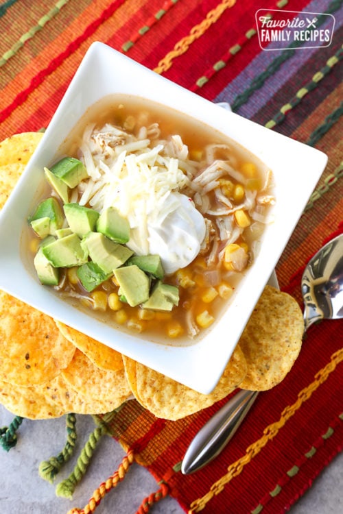 Chicken tortilla soup in bowl with sour cream and avocado with tortilla chips on the side.