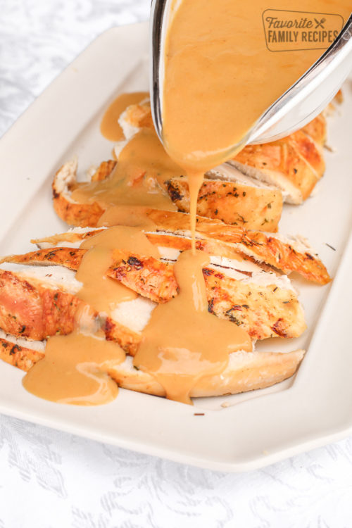 Turkey gravy in a white gravy boat being drizzled over roasted turkey breast slices