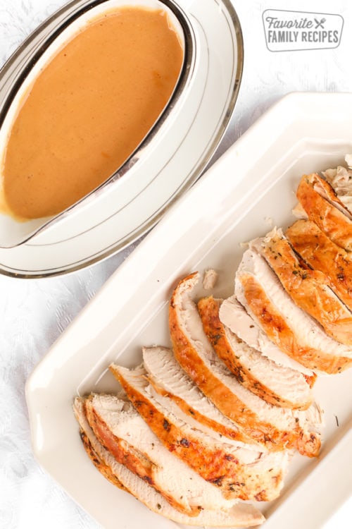 A gravy boat filled with turkey gravy next to a platter of sliced roasted turkey