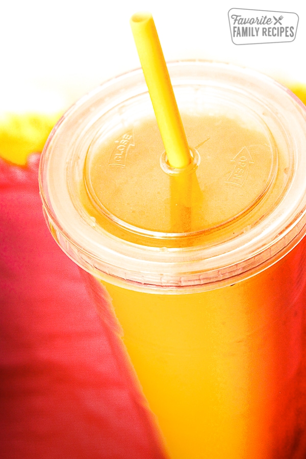A citrusy drink in a clear cup with a lid and straw.