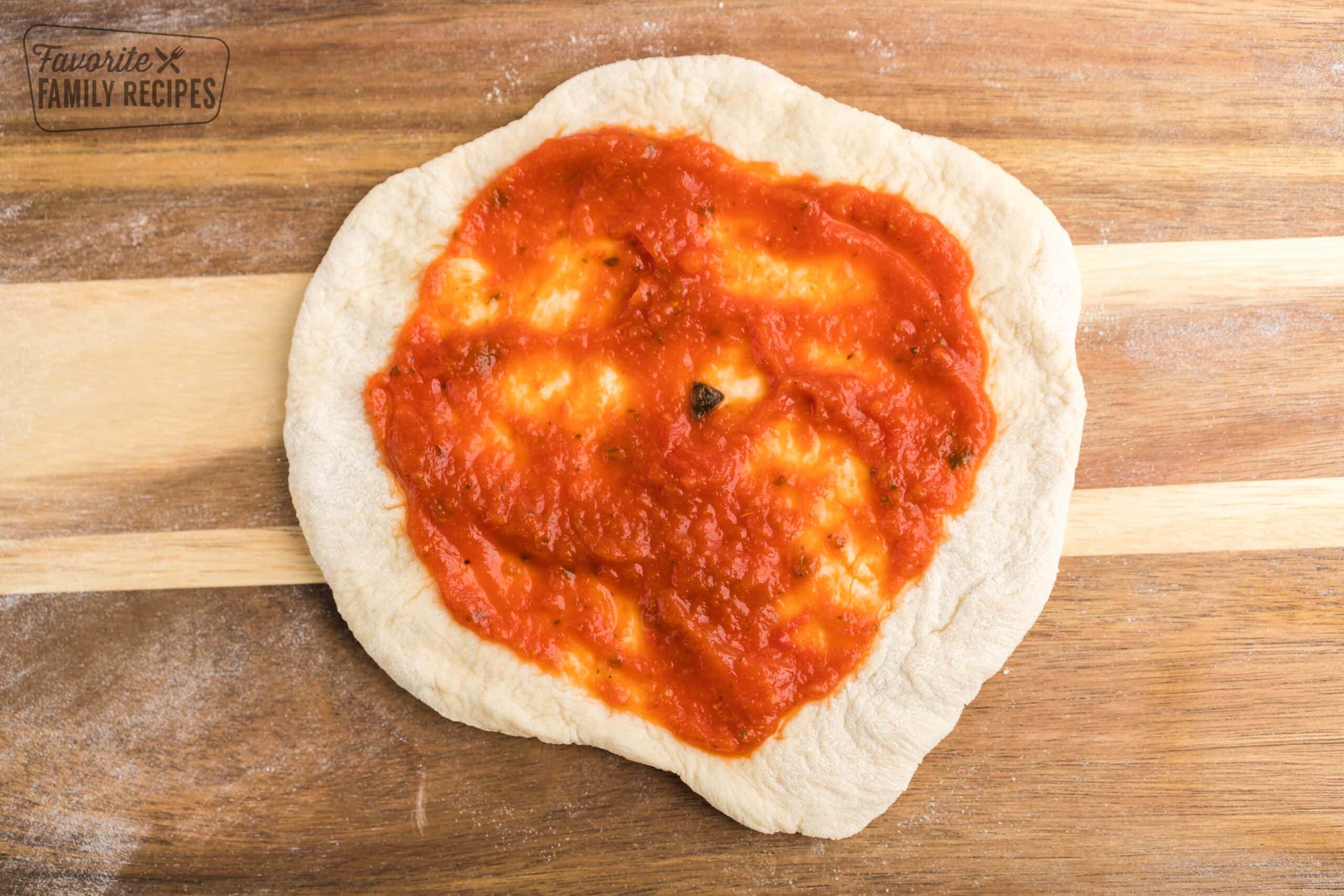Marinara sauce spread on pizza dough