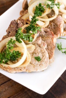 A tray of Crock Pot Cuban Pork Chops topped with onion slices and parsley