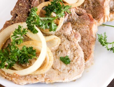 A tray of Crock Pot Cuban Pork Chops topped with onion slices and parsley