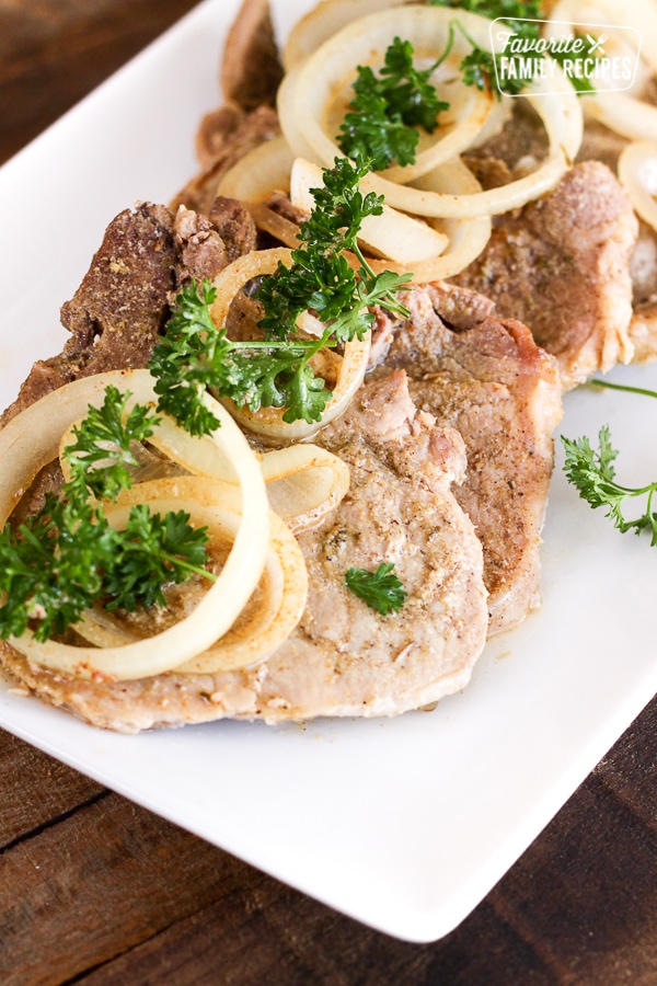 A tray of Crock Pot Cuban Pork Chops topped with onion slices and parsley.