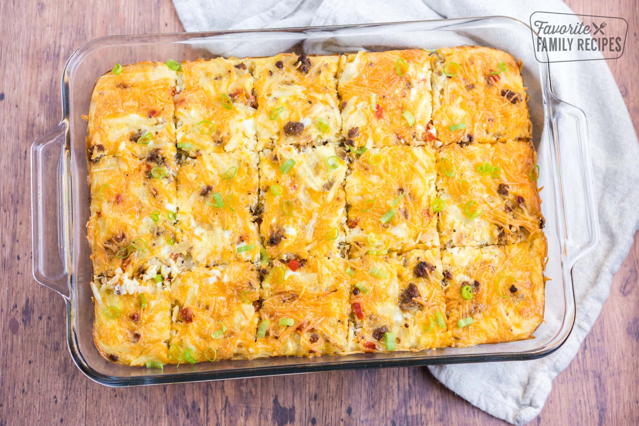 Breakfast casserole in a glass baking pan with eggs, hash browns, sausage, cheese, peppers, and green onion.
