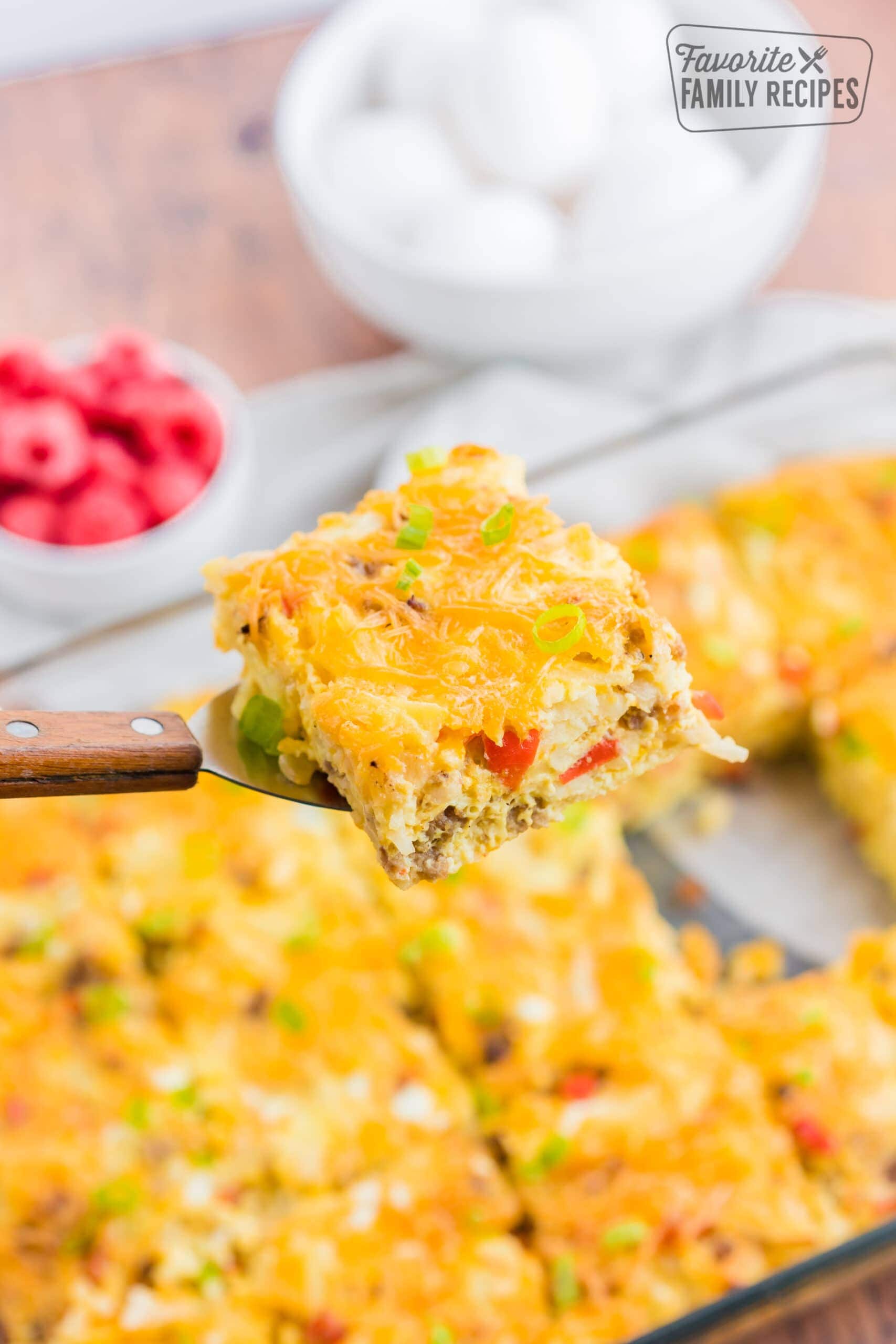 A slice of breakfast casserole being lifted out of a pan showing the eggs, sausage, peppers, and cheese.