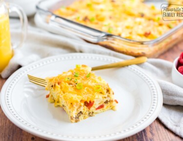 A slice of breakfast casserole made with egg, sausage, peppers, and melted cheese on a white plate
