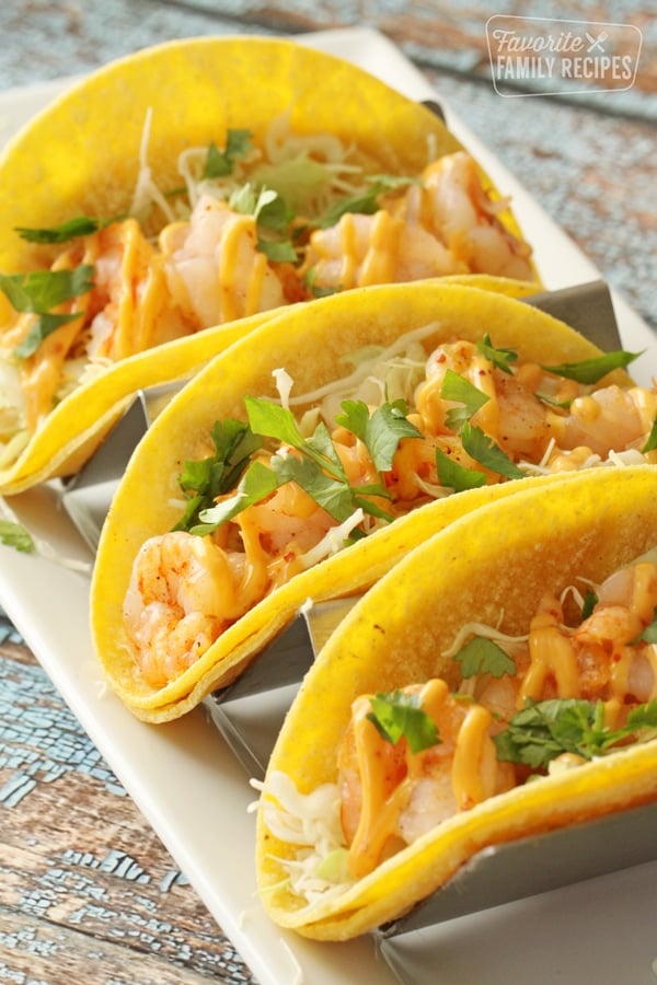 This Spicy Shrimp Taco Recipe makes the best meal or snack. Tender bite-size shrimp, crunchy cabbage and spicy sauce comes together in just minutes and disappears even faster! Three shrimp tacos on a plate.