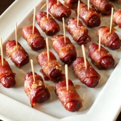 Bacon Wrapped Lil Smokies Appetizer with toothpicks in each one served on a white tray.