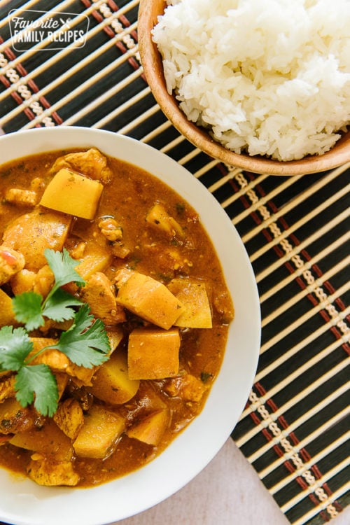 A close up view of chicken coconut curry with a bowl of jasmine rice on the side.