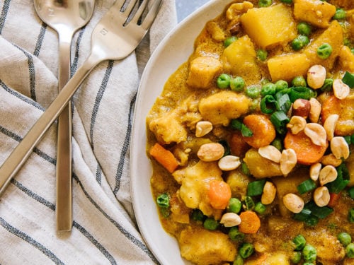 Coconut Curry Chicken with potatoes, carrots, and peas served in a white bowl with a fork and spoon to the side