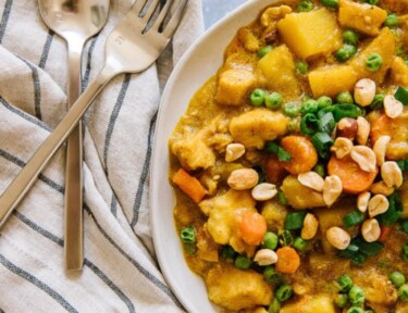 Coconut Curry Chicken with potatoes, carrots, and peas served in a white bowl with a fork and spoon to the side