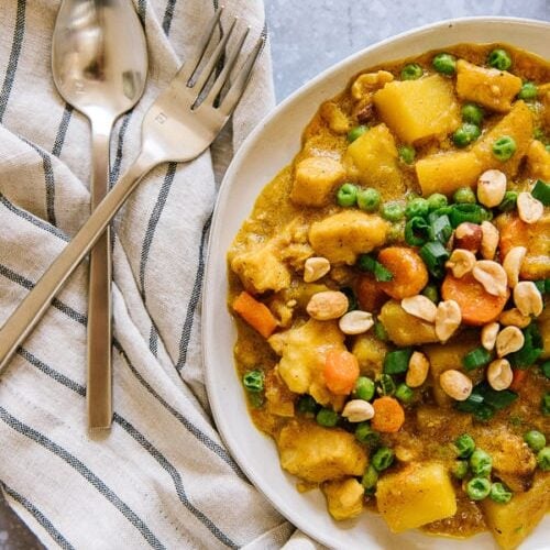 Coconut Curry Chicken with potatoes, carrots, and peas served in a white bowl with a fork and spoon to the side