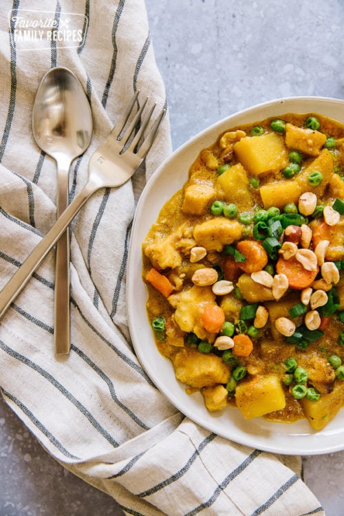 Coconut Curry Chicken with potatoes, carrots, and peas served in a white bowl with a fork and spoon to the side.