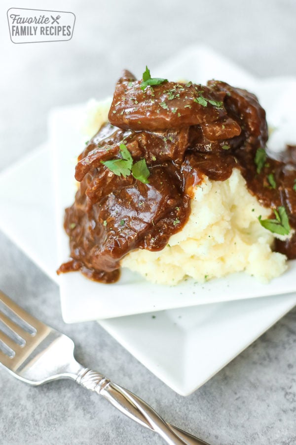 A close-up view of crockpot steak and gravy over mashed potatoes with parsley sprinkled on top