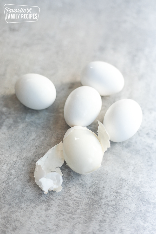 Five hard boiled eggs on a kitchen counter with one egg part way peeled
