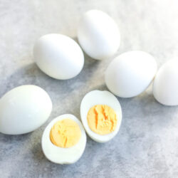 Easy Peel Hard Boiled Eggs on a kitchen counter with one egg peeled and cut in half with the yolk showing.
