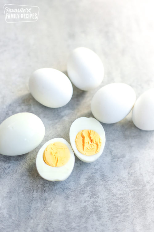 Easy Peel Hard Boiled Eggs on a kitchen counter with one egg peeled and cut in half with the yolk showing.