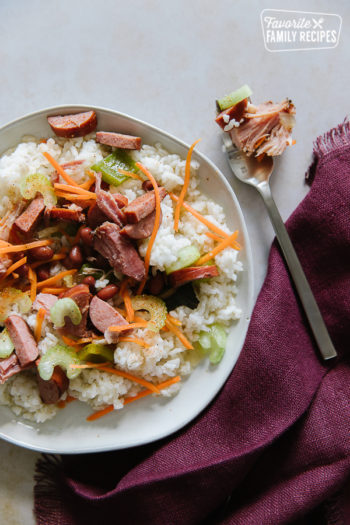 Red Beans and Rice is a hearty, flavorful recipe that comes together easily in the crockpot. Add ham and sausage and you've got a scrumptious supper or side dish! Red beans and rice on a white plate with a silver fork filled with red beans and rice.