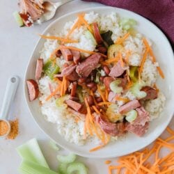 A round white plate of red beans and rice with carrots, celery, ham, and turkey sausage