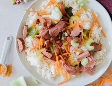 A round white plate of red beans and rice with carrots, celery, ham, and turkey sausage