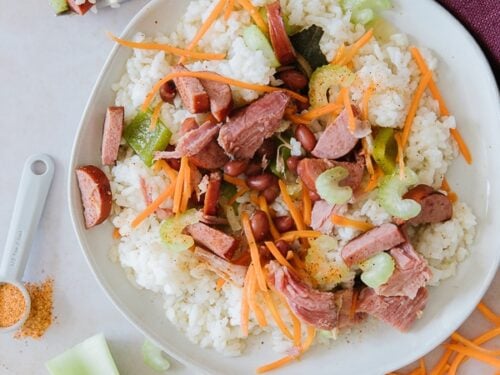 A round white plate of red beans and rice with carrots, celery, ham, and turkey sausage