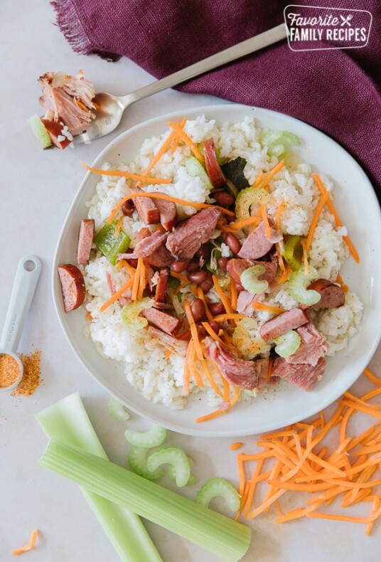 A round white plate of red beans and rice with carrots, celery, ham, and turkey sausage