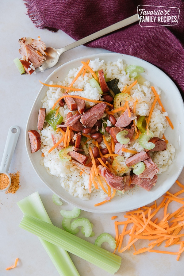 A round white plate of red beans and rice with carrots, celery, ham, and turkey sausage.