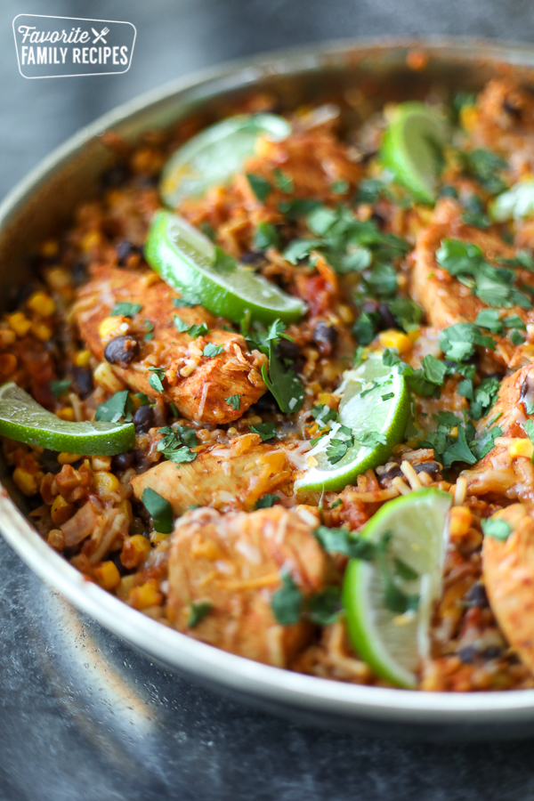 Spanish chicken with rice in a skillet garnished with lime wedges. 