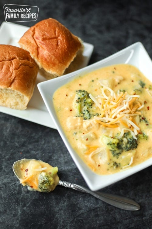 Broccoli cheese soup in a white bowl with two rolls on a white plate on the side. 