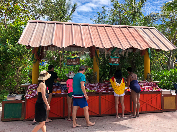 A little shop with sliced fruits and tourists looking.
