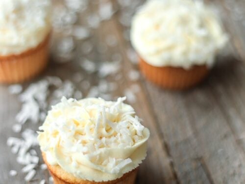 Coconut Cupcakes with coconut frosting on a wooden board with coconut flakes dusting the board