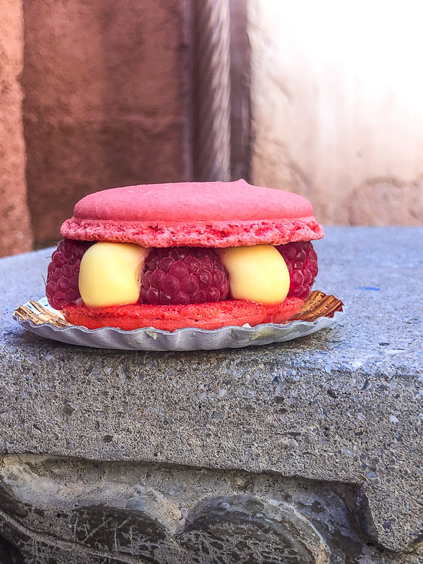 Macaron from Les Halles Boulangerie-Patisserie, a dark pink colored macaroon filled with fresh raspberries and lime cream sitting on a stone bench