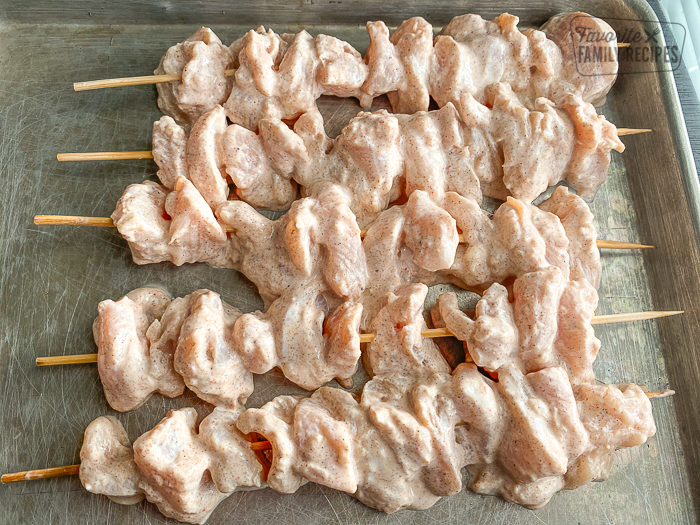 Uncooked chicken on skewers being prepared to grill.