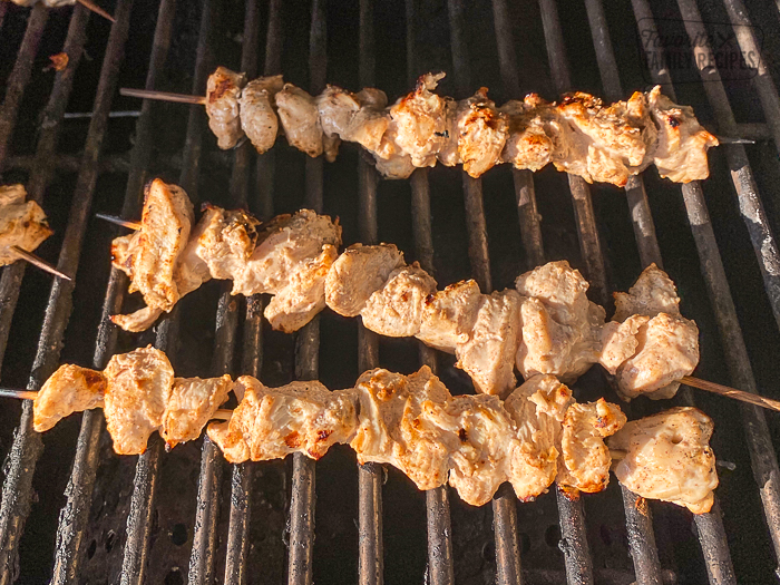 Chicken skewers cooking on grill.