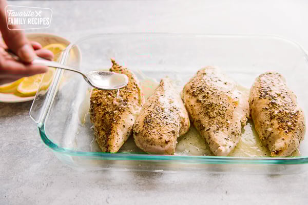 Spooning sauce over seasoned poultry in a baking pan
