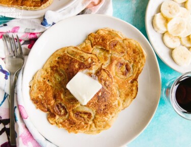 Two banana pancakes on a white plate with butter melting on top