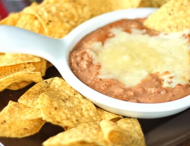 Cheater Restaurant Style Refried Beans in a white bowl surrounded by tortilla chips.