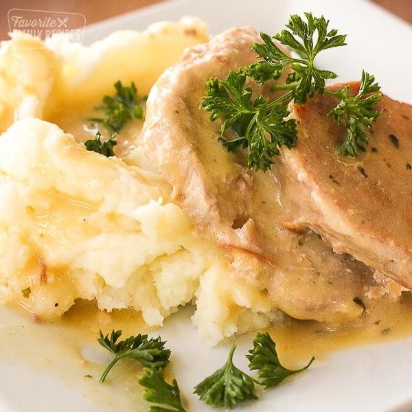 Easy Crock Pot Pork Chops with sauce and mashed potatoes on a white plate.
