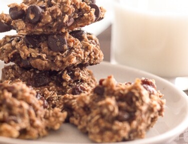 Healthy Oatmeal Cookies stacked on a white plate with a glass of milk in the background.