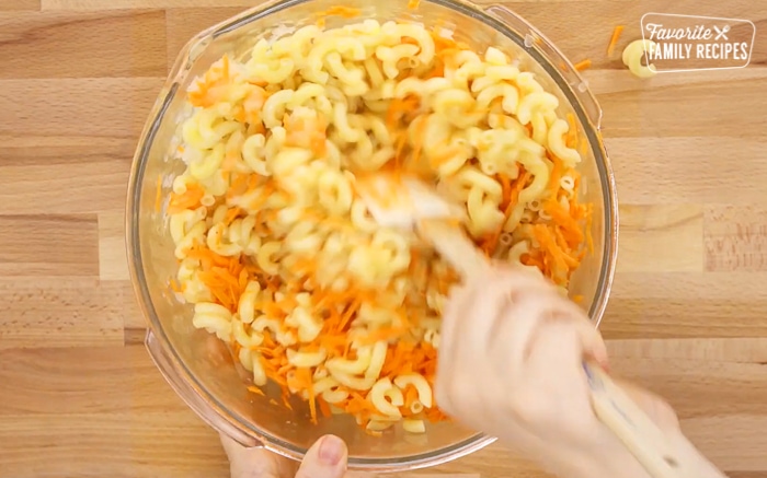 Hawaiian macaroni salad in a glass bowl being mixed together with a spatula.