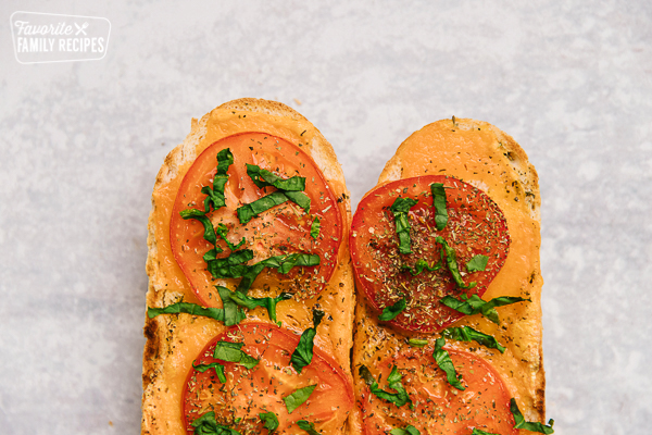 Two slices of Cheesy Italian Bread with tomatoes and fresh basil