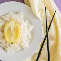 A bowl filled with lemon rice with chopsticks and a yellow napkin to the side