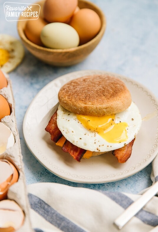 A plated egg McMuffin with a bowl of eggs to the side
