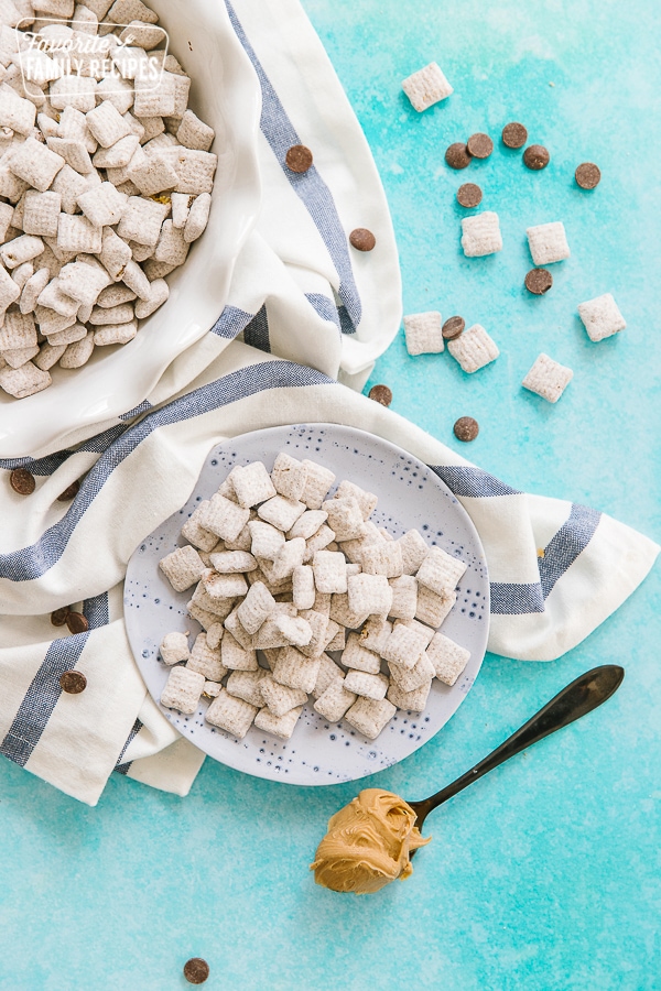 Muddy Buddies on a plate surrounded by chocolate chips and a spoonful of peanut butter.