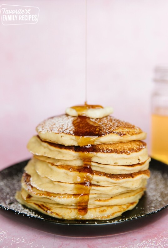 A stack of pancakes from scratch on a black plate with syrup pouring over them