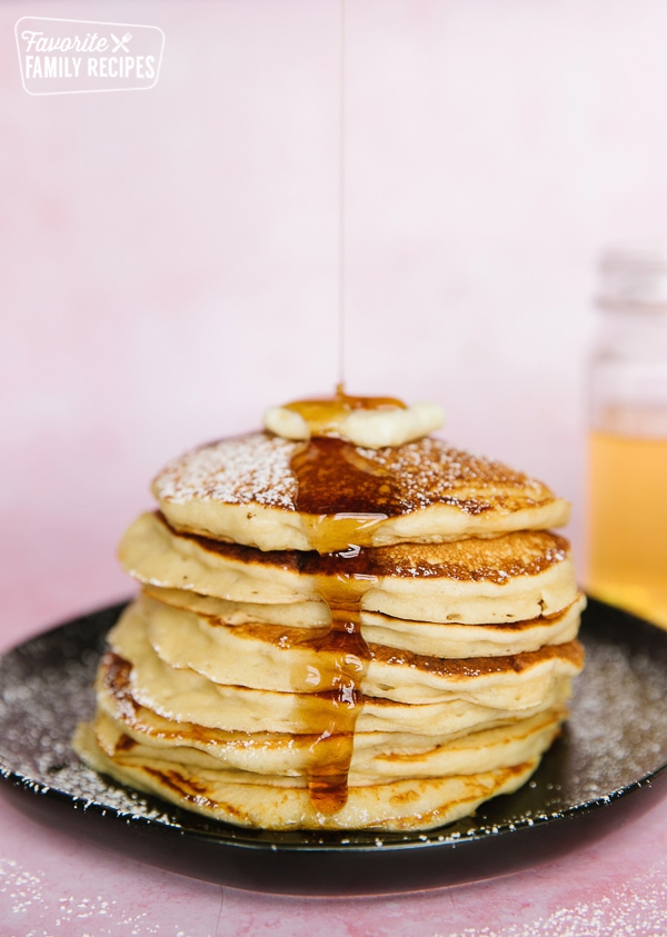 A stack of pancakes from scratch on a black plate with syrup pouring over them
