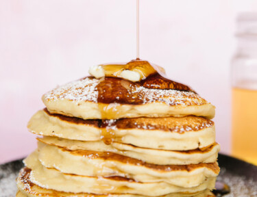 A stack of pancakes with syrup being poured on top