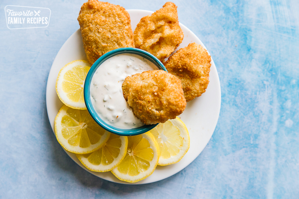 A piece of fried fish being dipped into a bowl of tartar sauce