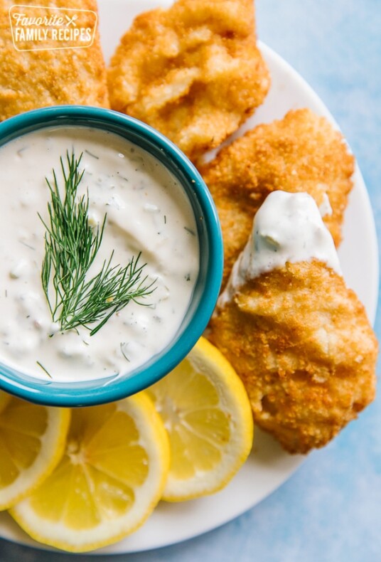 A bowl of tartar sauce surrounded by fried fish and lemon wedges